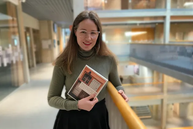 Woman holding thesis book in a hall way