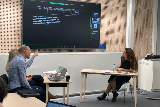 Kvinna vid skrivbord mittemot man och kvinna vid annat bord